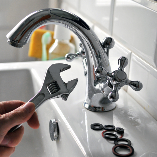 A person is fixing a faucet with a wrench