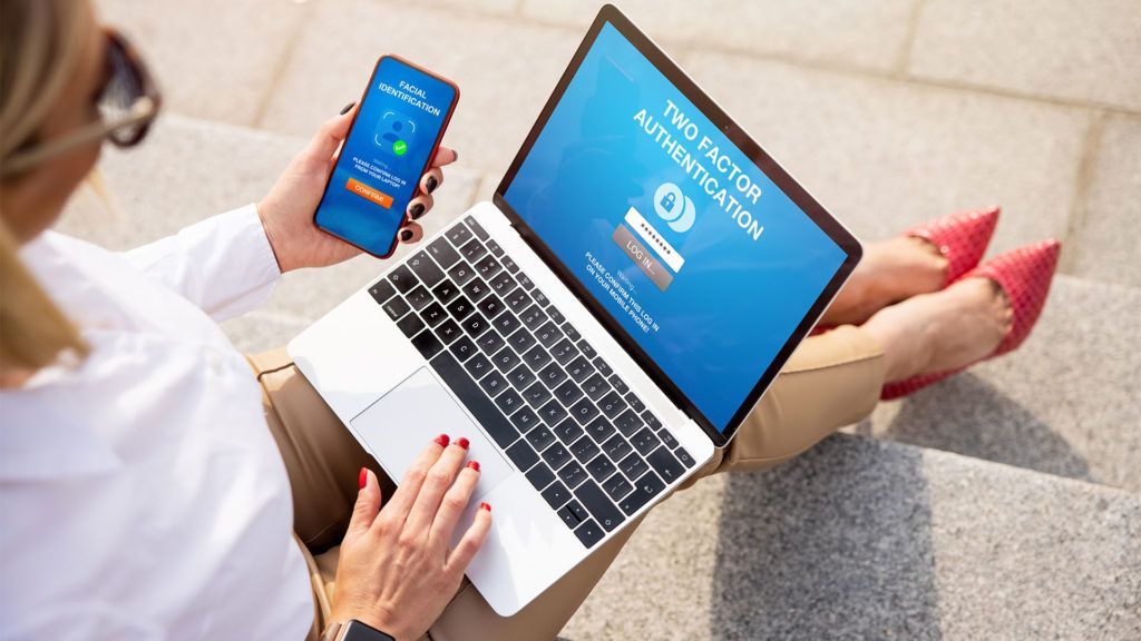 Mulher usando laptop e celular para autenticação de dois fatores ao ar livre, sentada em uma escada.