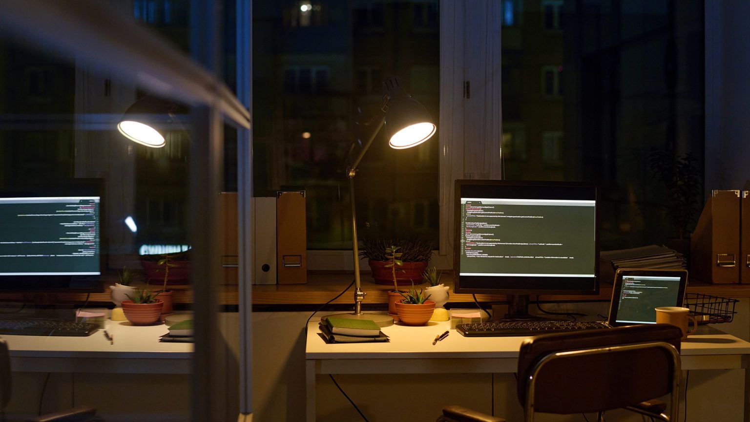 Computadores em escritório à noite exibindo códigos, representando cibersegurança e resposta ao inci