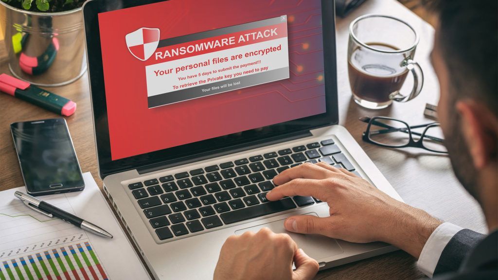 Homem em frente a um laptop sofrendo um ataque de ransomware na tela, indicando uma ameaça à segurança cibernética.