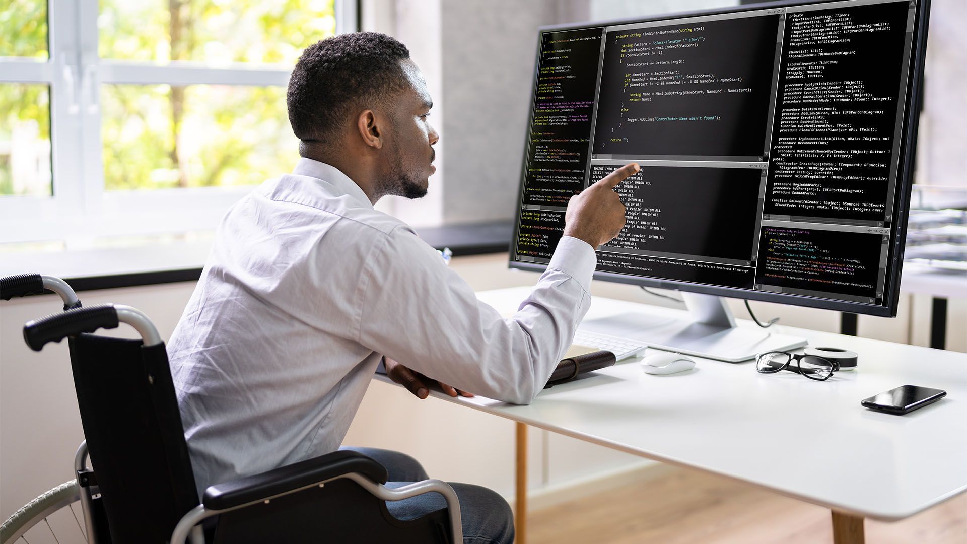 Homem em cadeira de rodas programando em um computador com várias telas.