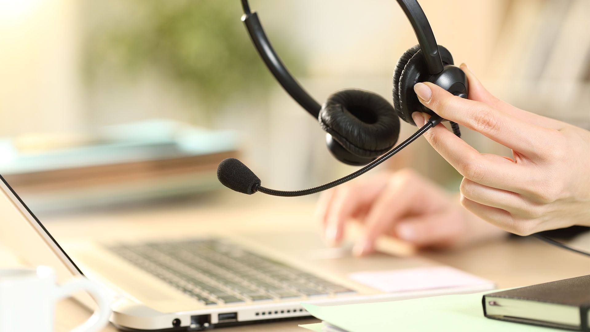 Pessoa segurando um fone de ouvido perto de um laptop, preparando-se para uma chamada em um ambiente de escritório.