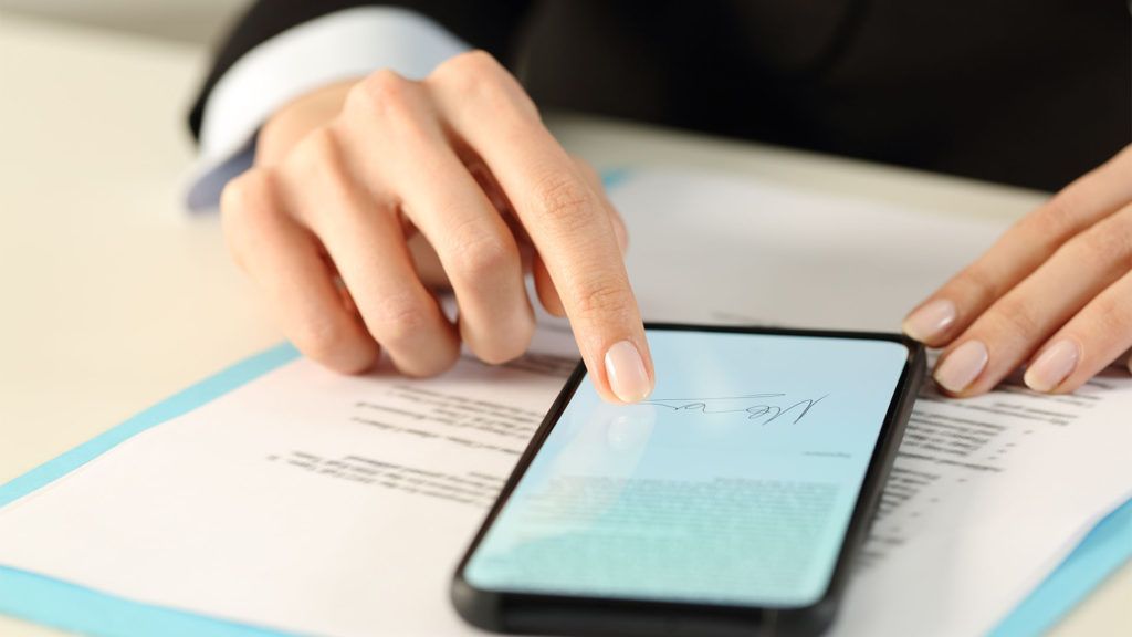 Mão de pessoa usando um smartphone sobre documentos.