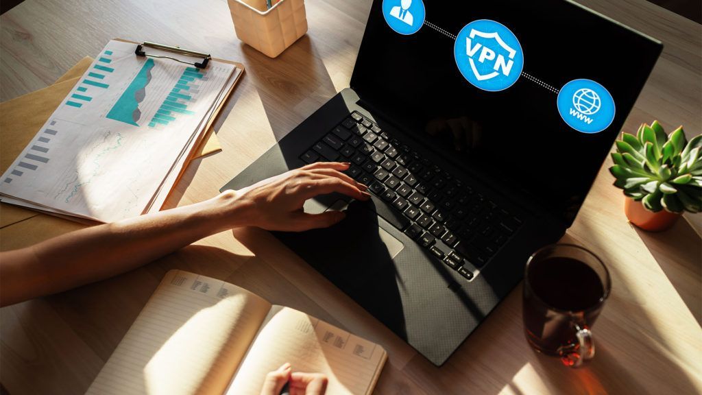 Pessoa usando laptop com ícone de VPN na tela; ambiente de escritório.