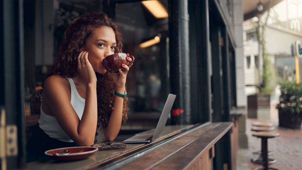 Mulher tomando café em um café ao ar livre com um laptop.