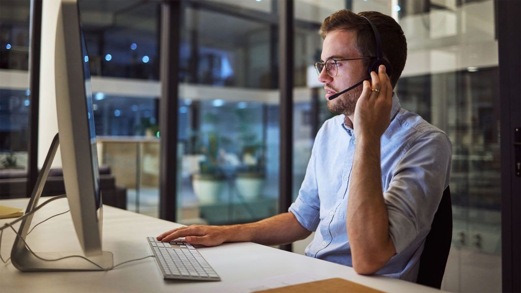 Homem usando fones de ouvido, trabalhando em um computador à noite em um escritório.