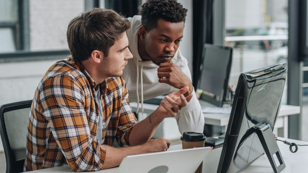 Dois homens olhando para a tela do computador, discutindo detalhes em um escritório.
