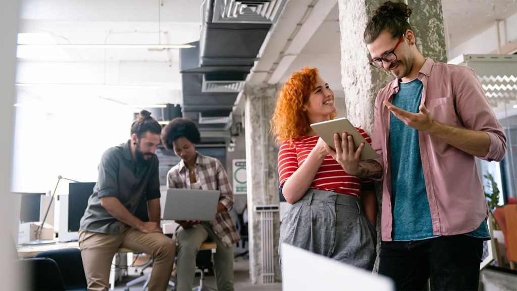 Colegas de escritório colaborando em laptops e tablets em um espaço aberto e moderno.