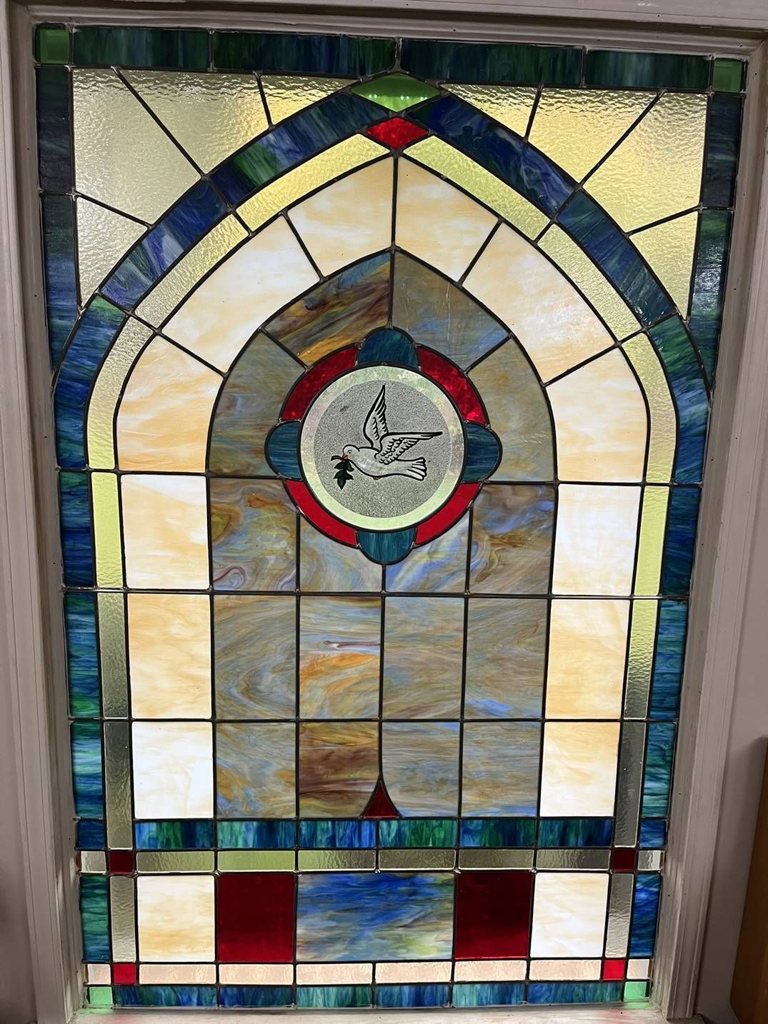 Stained glass window with arched top; features circular emblem, blue, red, yellow and clear glass panes.