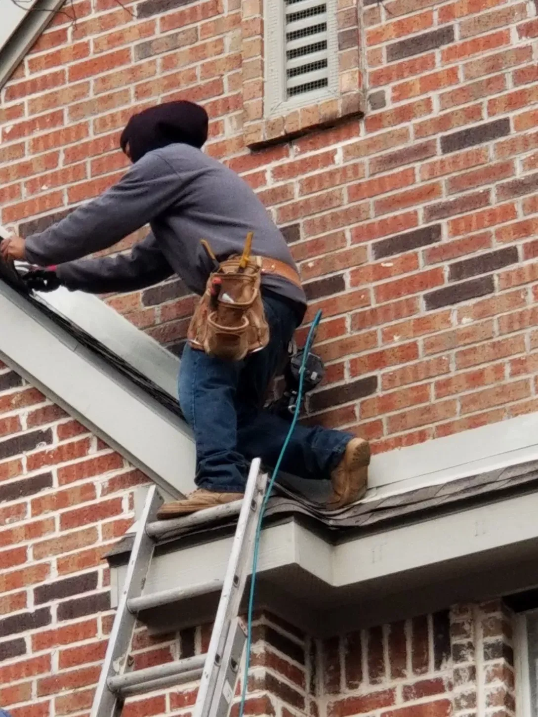 A man is standing on a ladder on the side of a brick building.