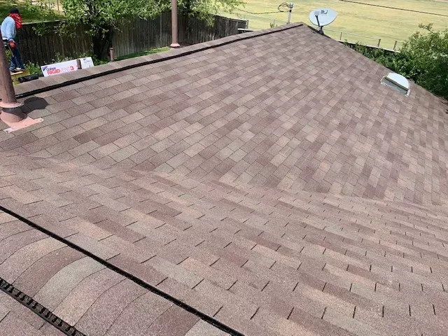 A man is standing on the roof of a house with a satellite dish on it.