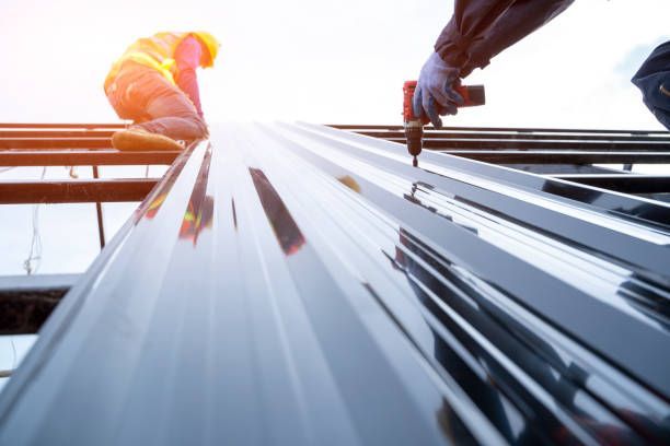 Two construction workers are working on a metal roof.