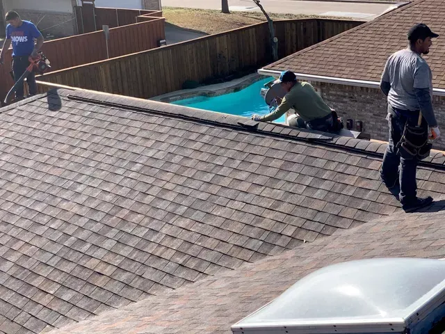 Two men are working on the roof of a house next to a pool.