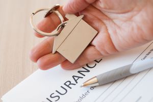 A person is holding a house key on top of a insurance form