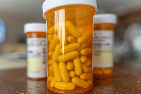 Orange pill bottles with yellow capsules on a wooden surface, focus on a front bottle