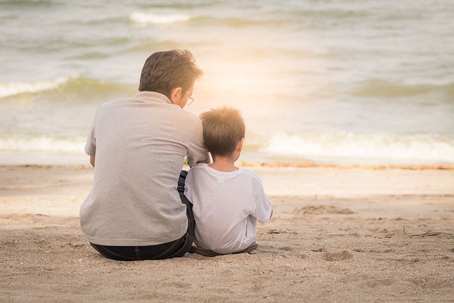 A man and a boy are sitting on the beach looking at the ocean.