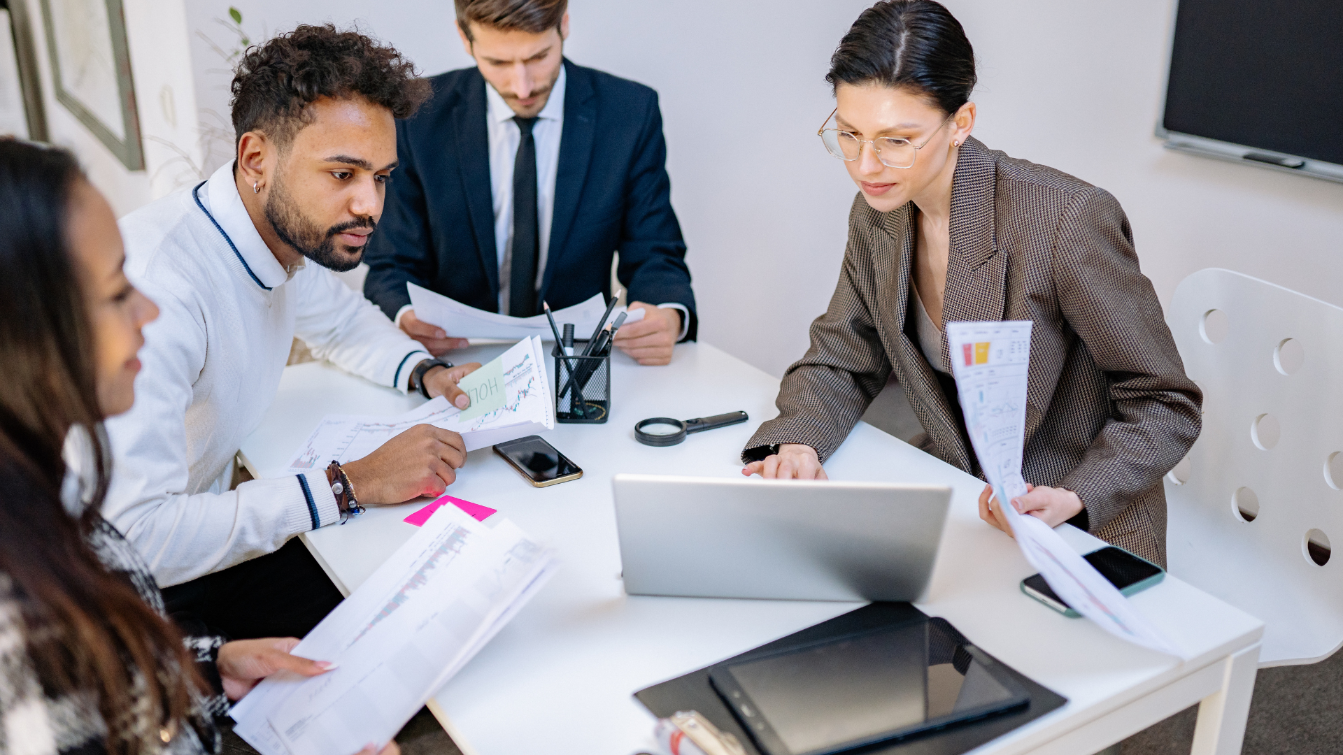 Business team at a table, discussing documents and a laptop in a bright office.