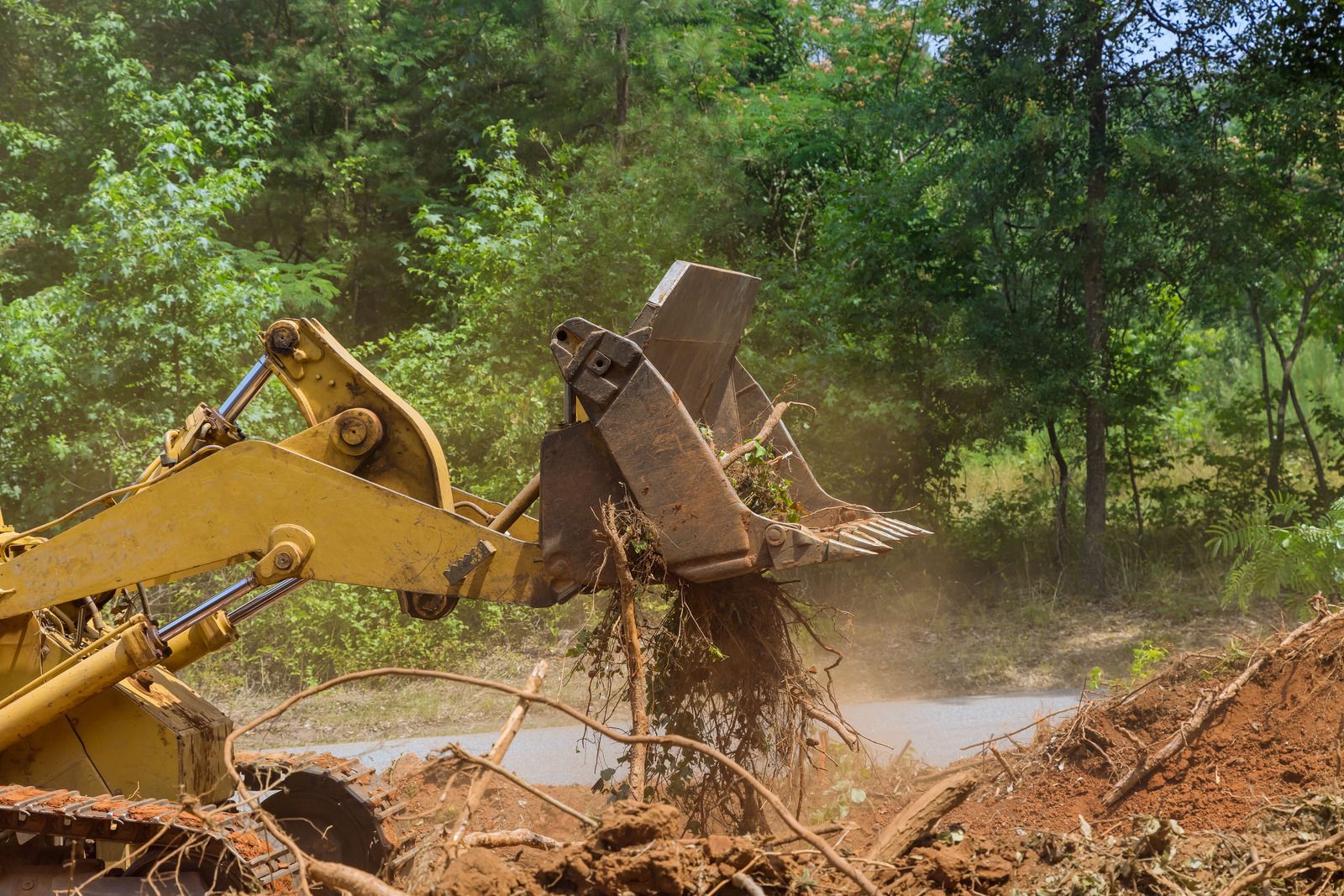Yellow bulldozer digging up dirt and tree roots in a wooded area.
