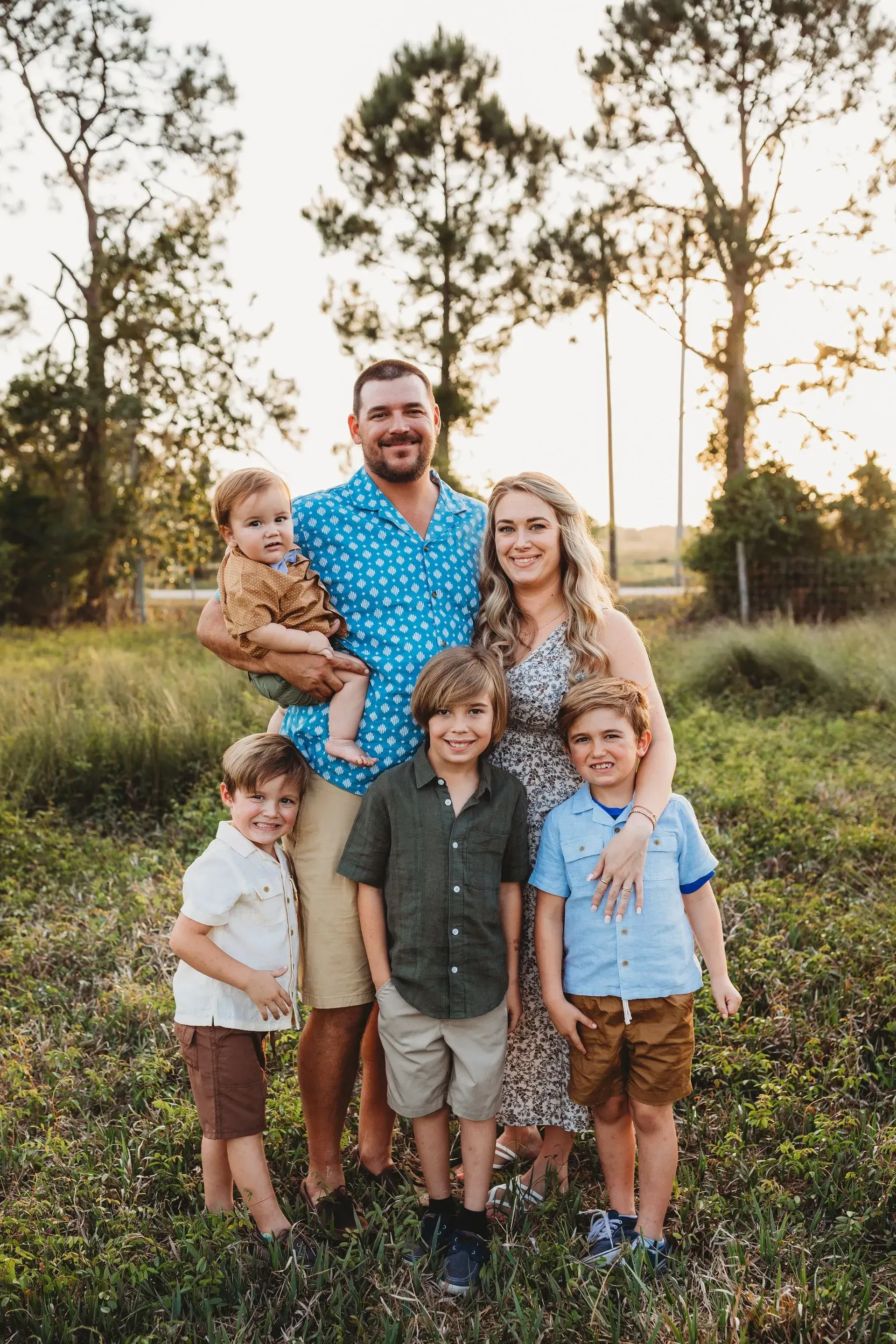 Arborist in harness atop a tree stump under cloudy sky. Bushes and building visible.