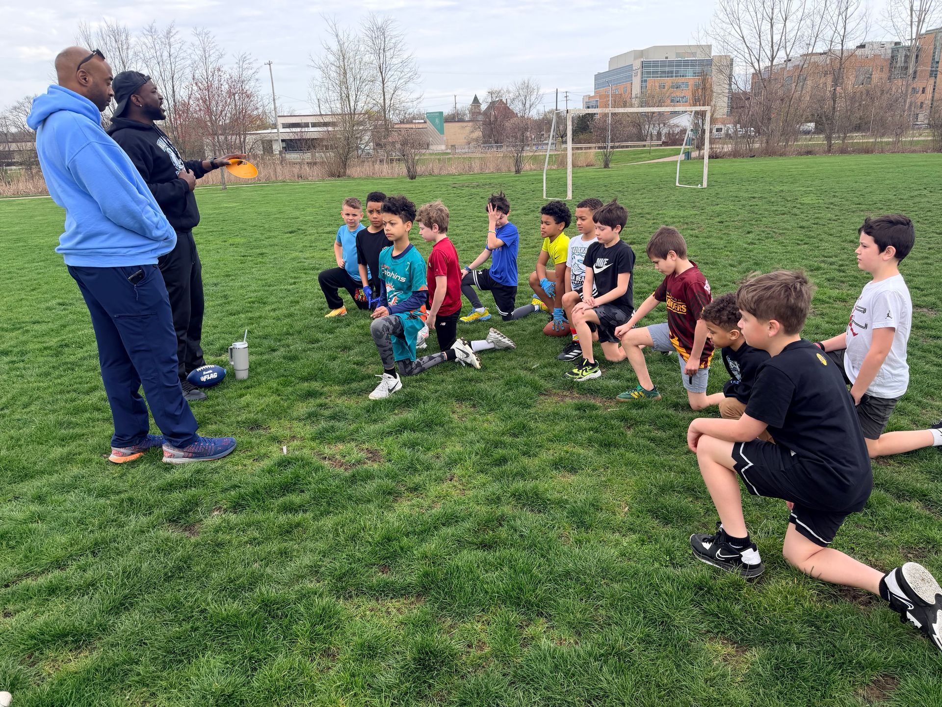 Children doing outdoor exercises on a grassy field with two coaches nearby