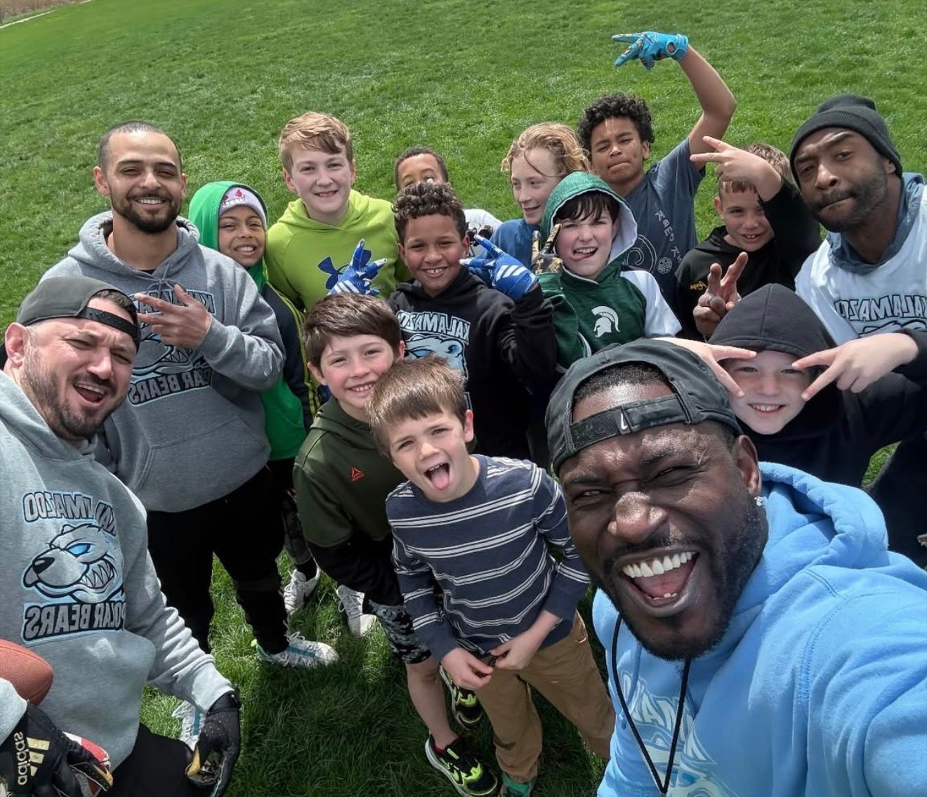 Smiling group taking a selfie outdoors on a grassy field, wearing casual clothes and hoodies
