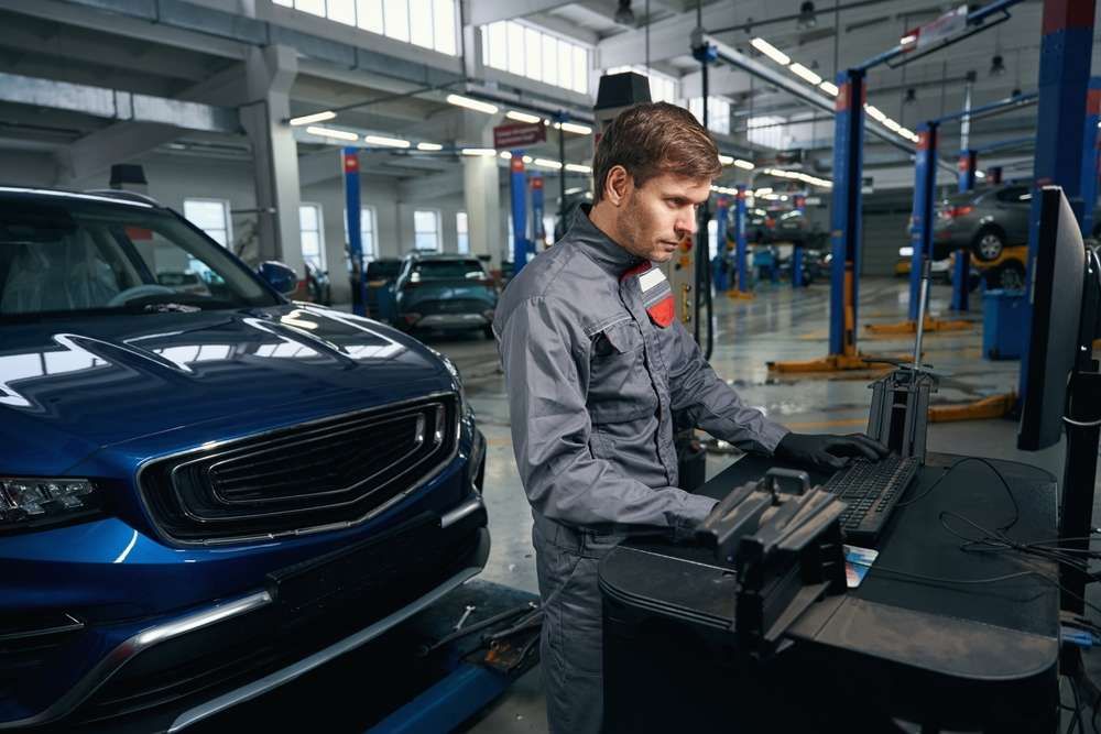 A Man Is Working On A Computer In A Garage Next To A Car — Prestige Automotive NT In Yarrawonga, NT