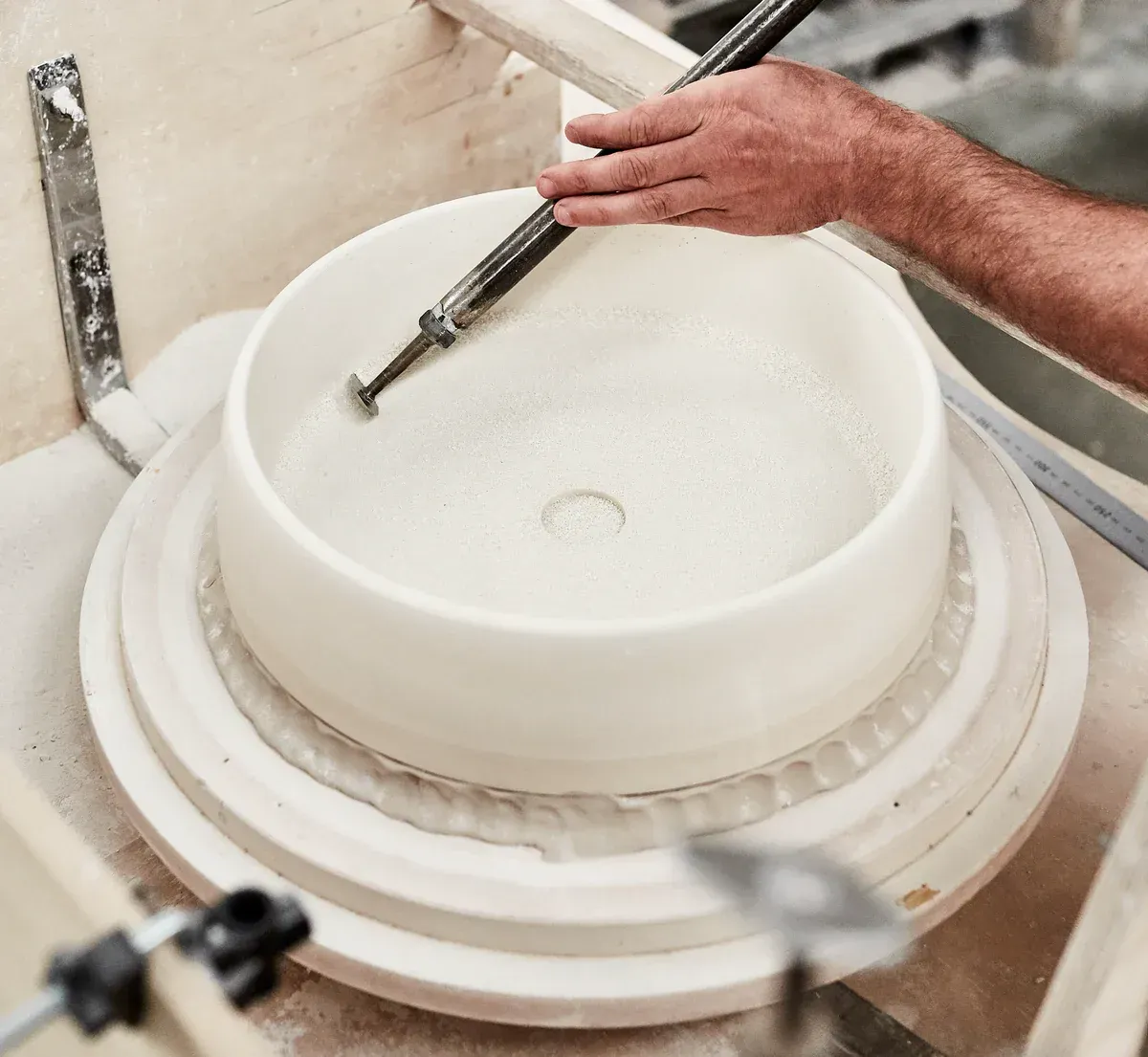 Person shaping a white ceramic sink in a workshop using a tool — Stone Arc in Kincumber, NSW