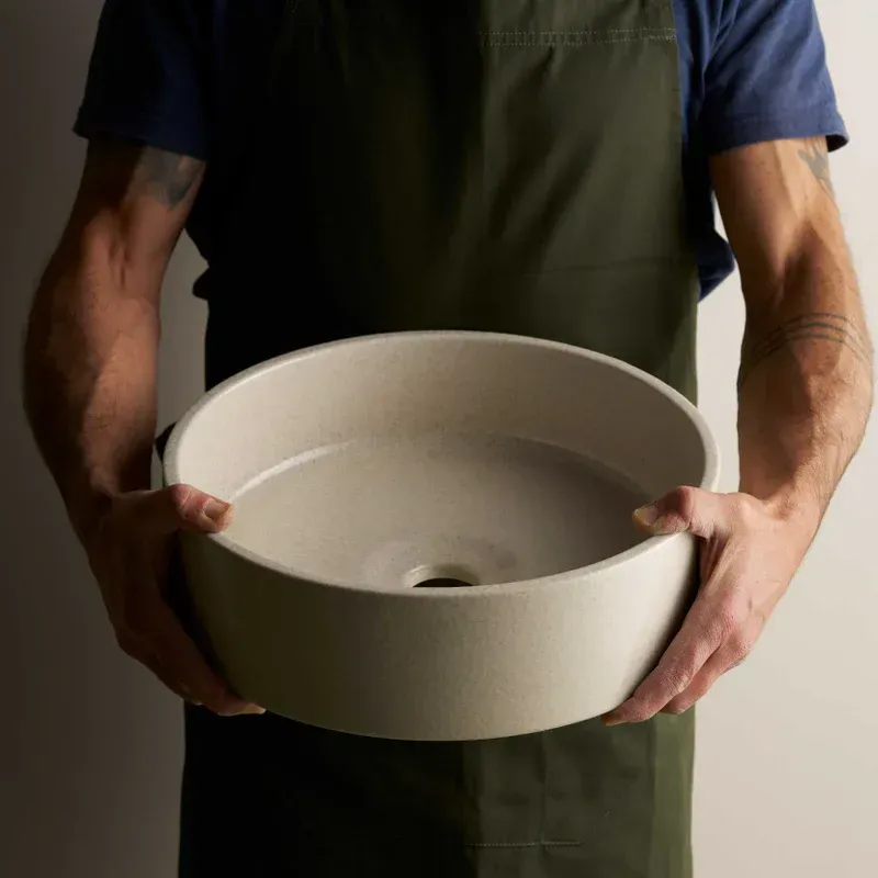 Person holding a round, beige ceramic sink. They wear a green apron and blue shirt — Stone Arc in Kincumber, NSW