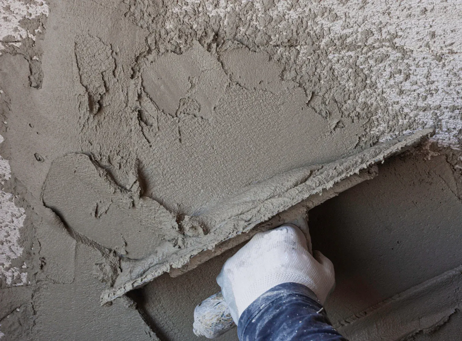 A person is using a trowel to spread concrete on the ground.