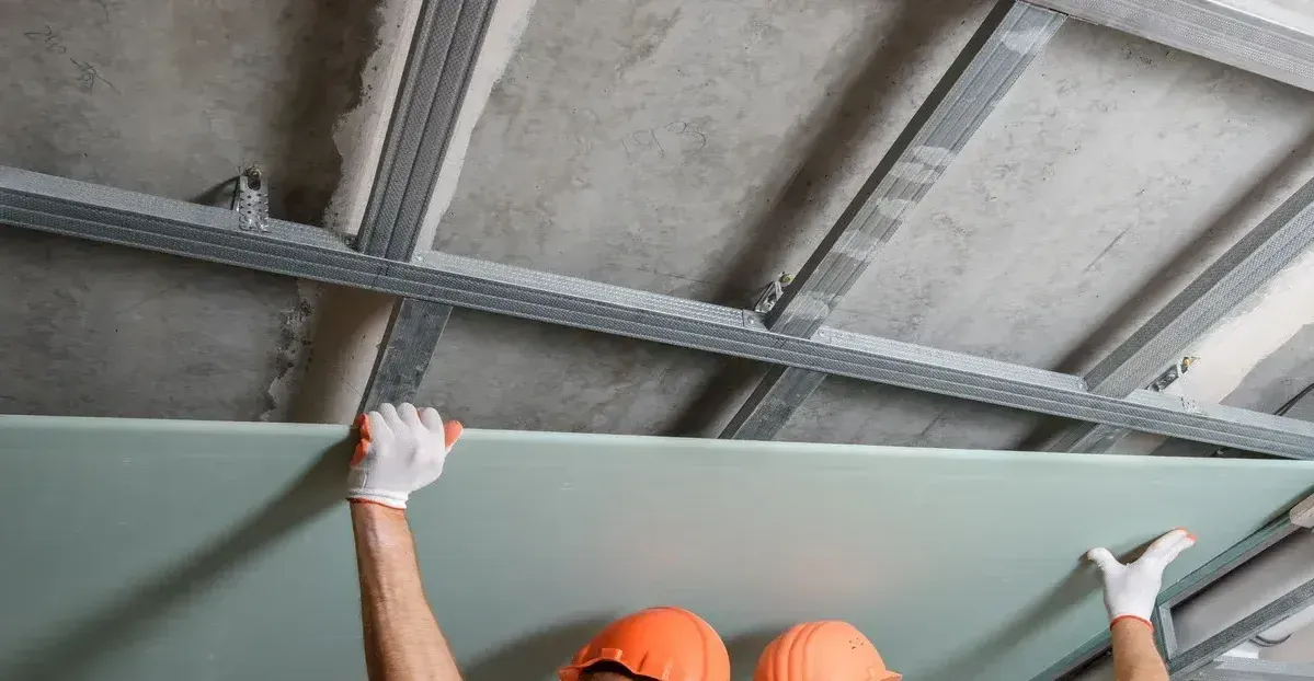 A man is hanging a piece of drywall from the ceiling.
