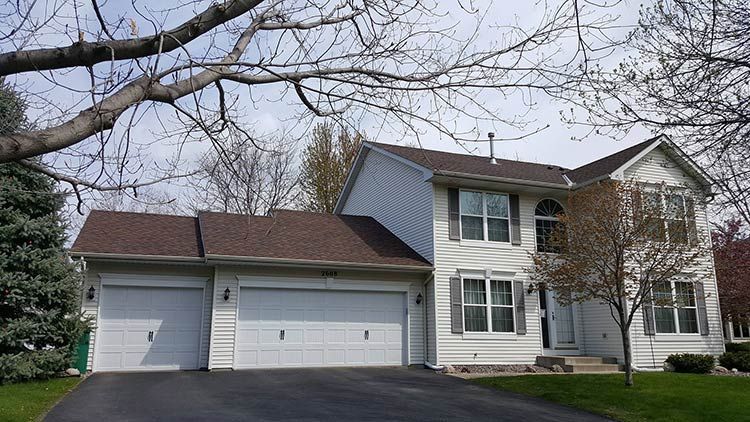 A large white house with a brown roof and two garage doors.