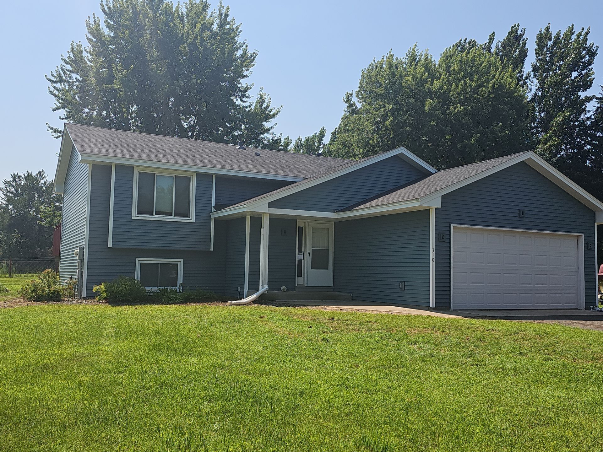 A blue house with a white garage door is sitting on top of a lush green field.