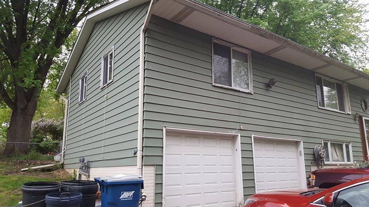 A green house with two garage doors and a red car parked in front of it.