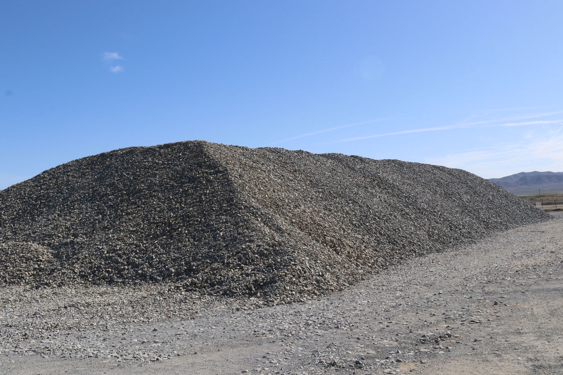 A large pile of gravel is sitting in the middle of a dirt field