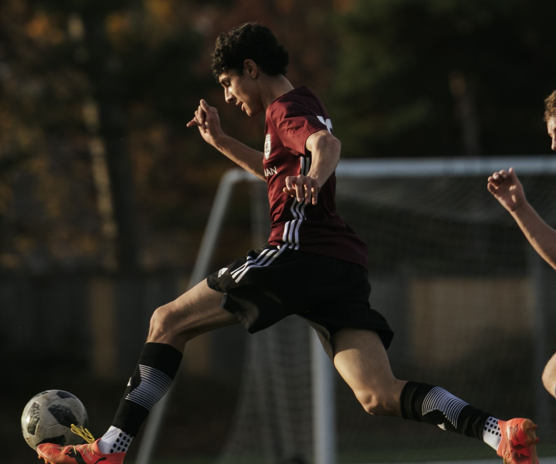 Soccer player in red and black uniform kicks a ball on the field at night