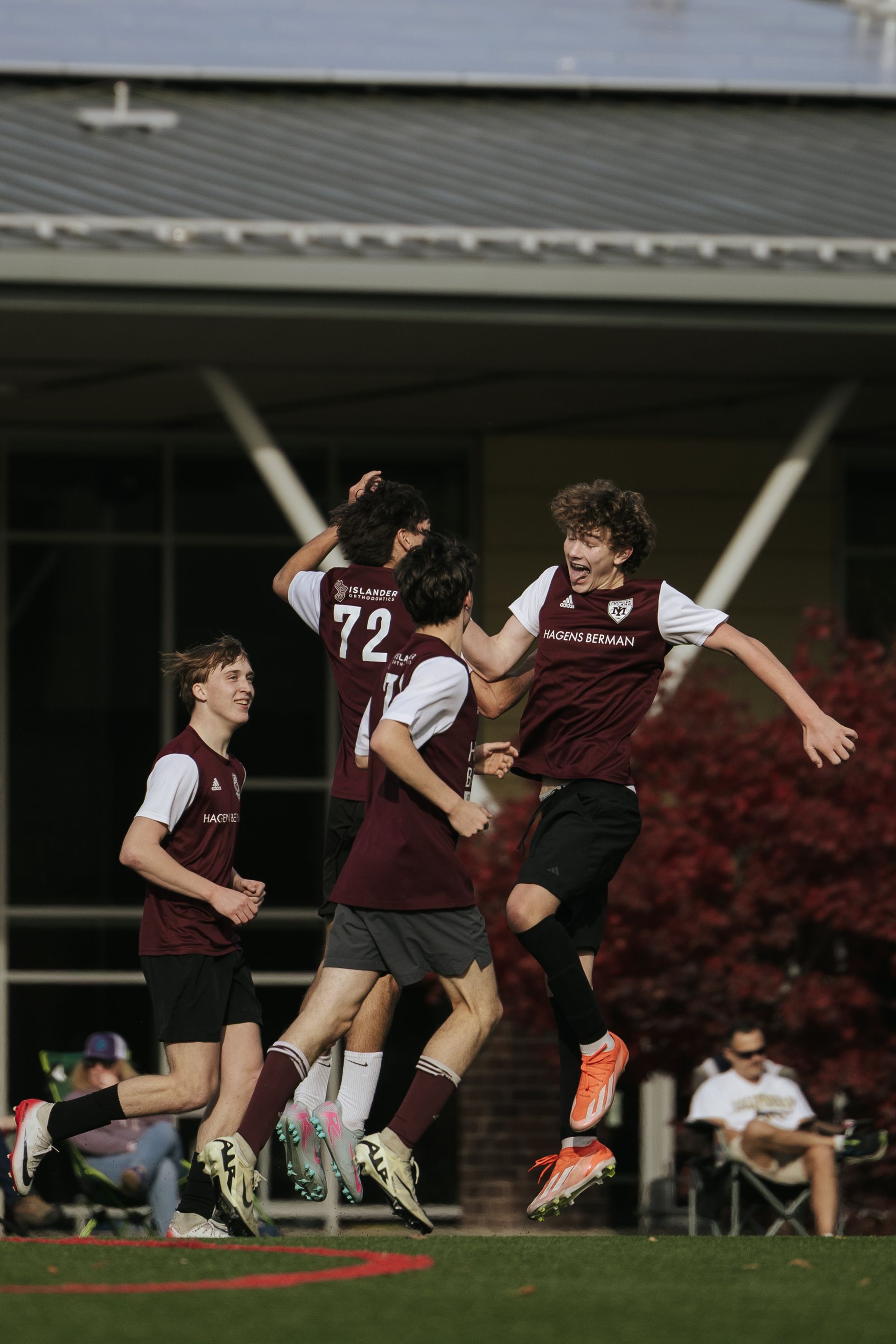 Soccer players in maroon jerseys jump and celebrate on the field at night