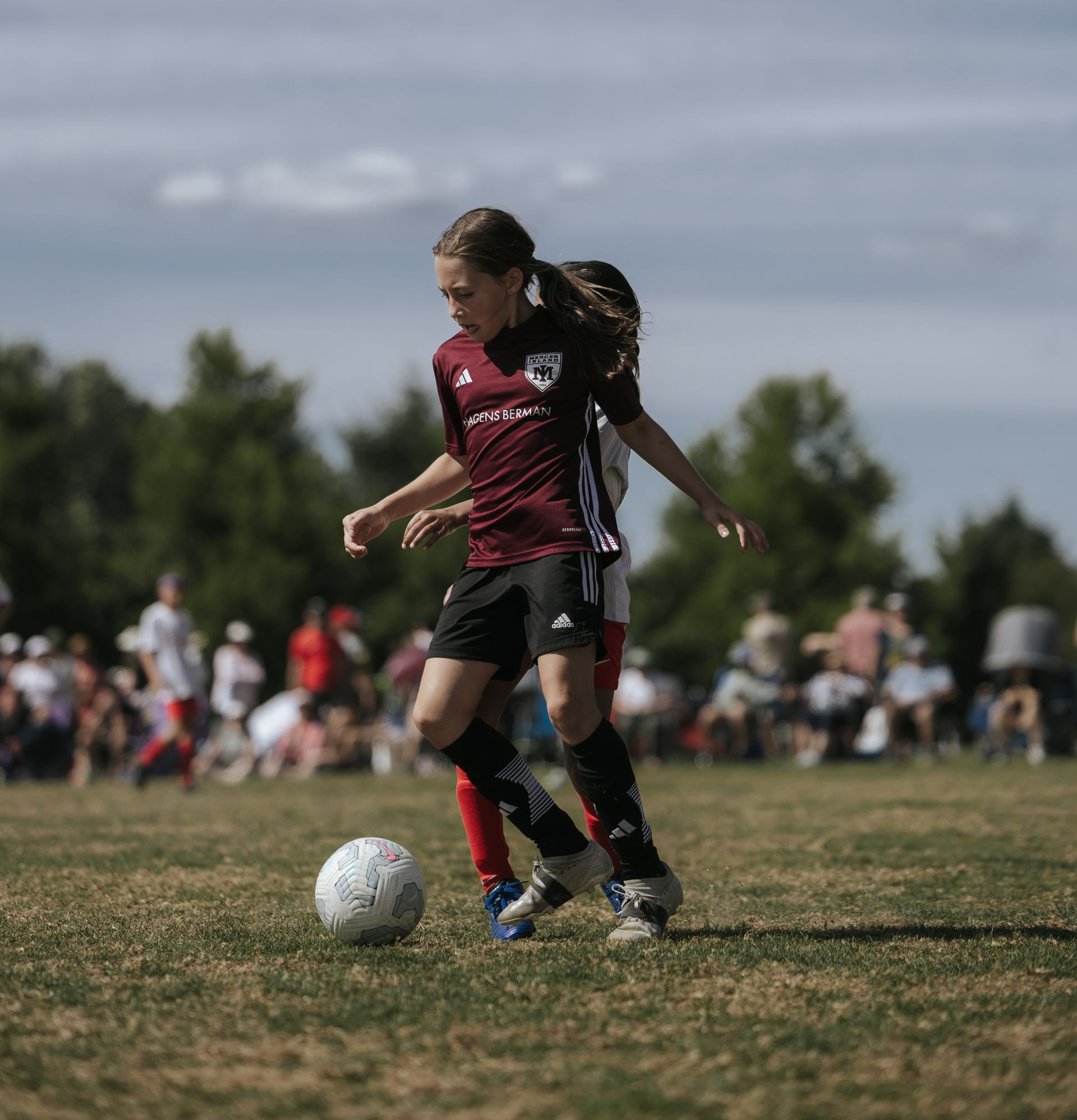 Two soccer players in maroon and black contest the ball on a grassy field
