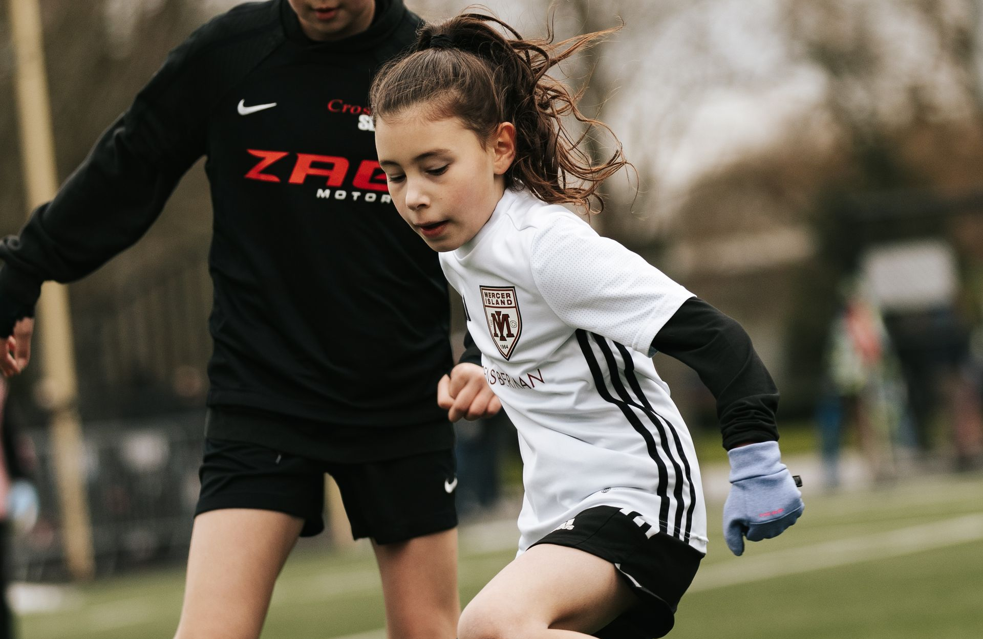 Two soccer players in black and white uniforms contest the ball on a field