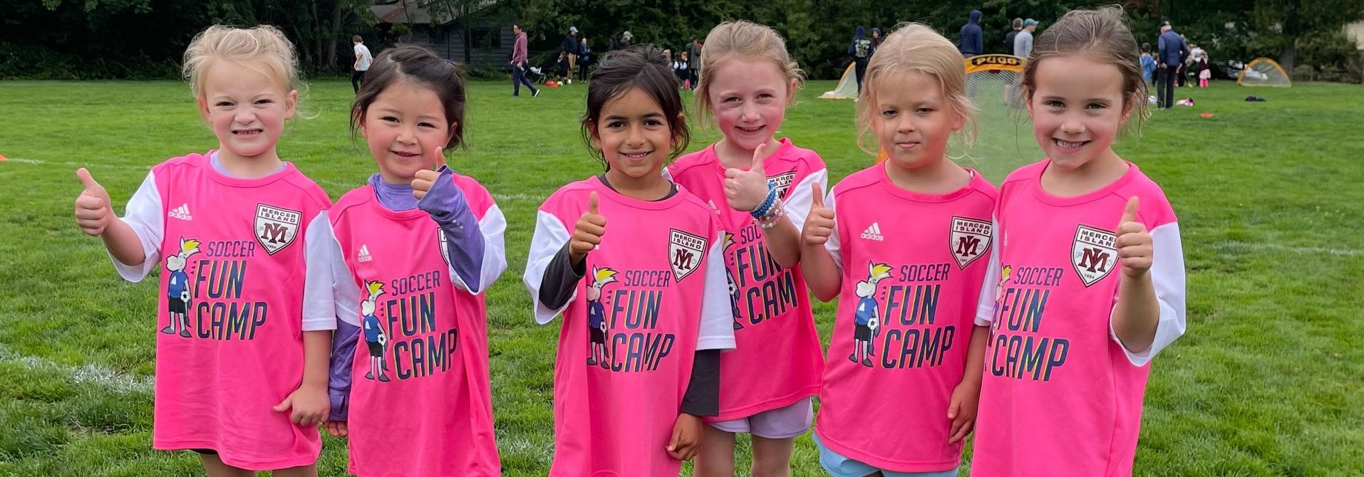 Six children in matching bright pink shirts standing on grass outdoors, smiling at the camera