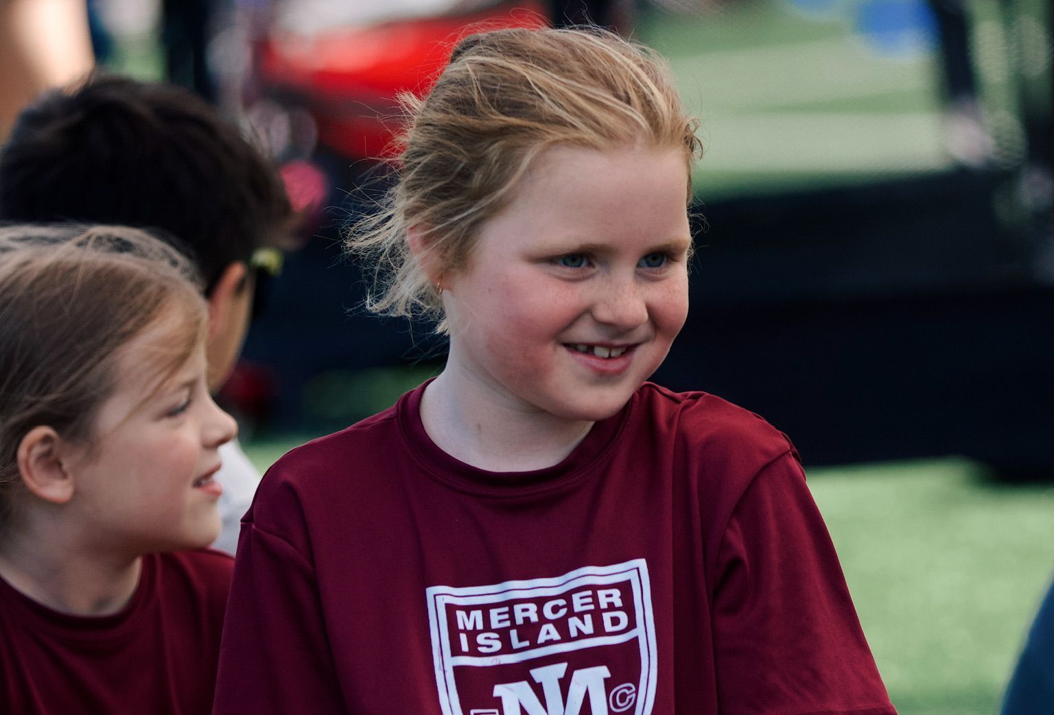 Two smiling children outdoors, one in a maroon Mercer Island shirt.