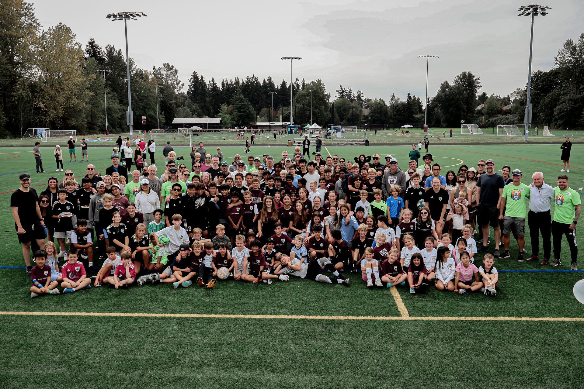 Large group posing on a soccer field, with people seated and standing in rows on green turf.