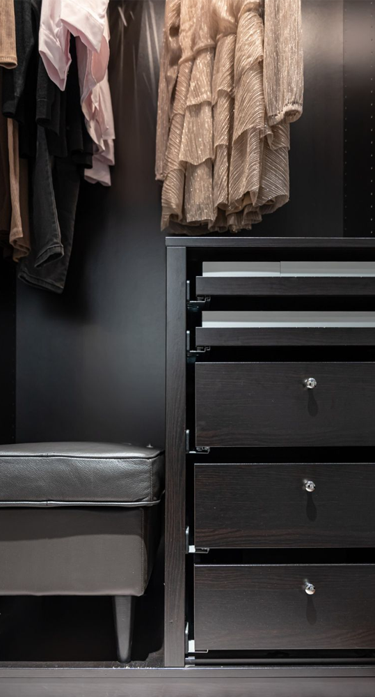 Closet with dark wood drawers, clothes hanging, and a gray bench.