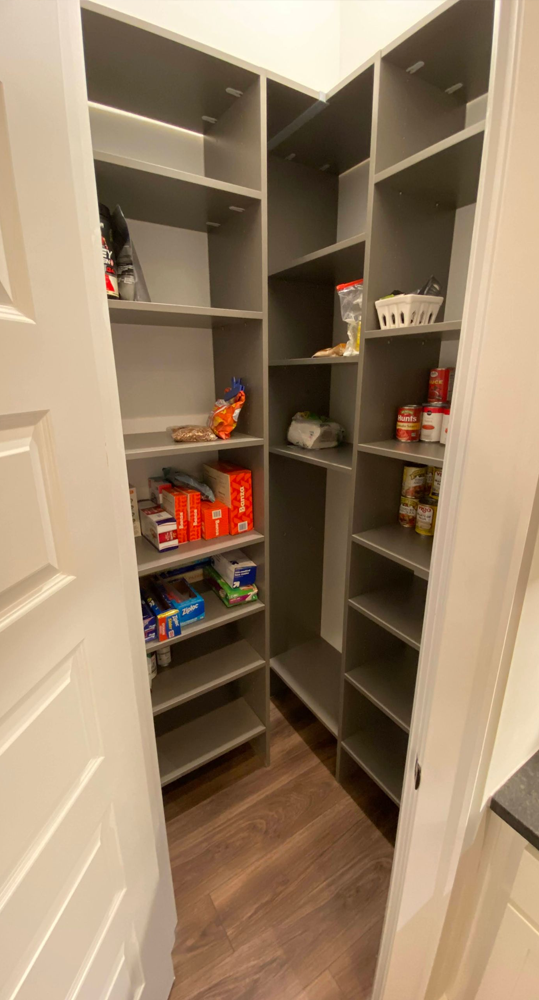 Walk-in pantry with gray shelves and various food items on them. Dark wood floor.