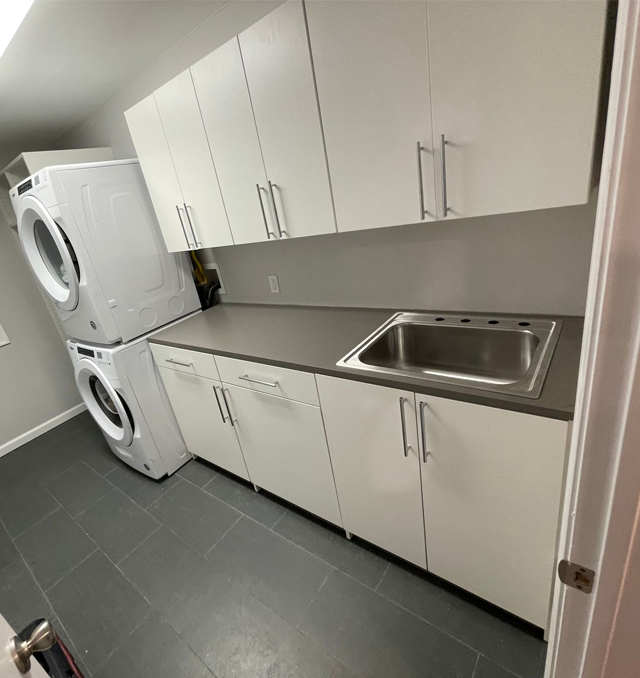 Laundry room with stacked white washer and dryer, white cabinets, and a sink.