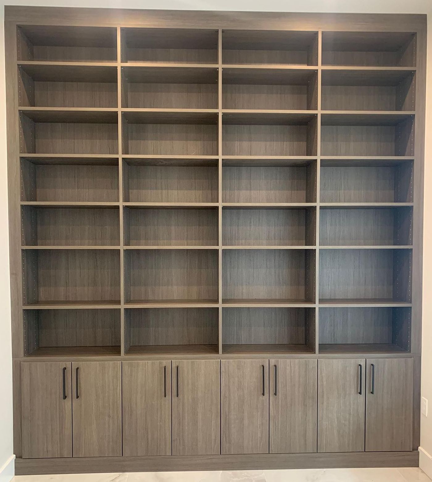 Built-in wooden bookshelf with numerous open shelves and lower cabinets, neutral wood color.