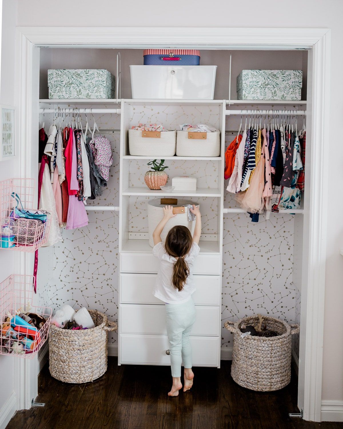 Girl reaching for a box in a neatly organized closet with clothes and storage baskets.