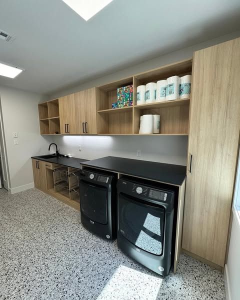 Laundry room with black appliances, light wood cabinets, and terrazzo floor.