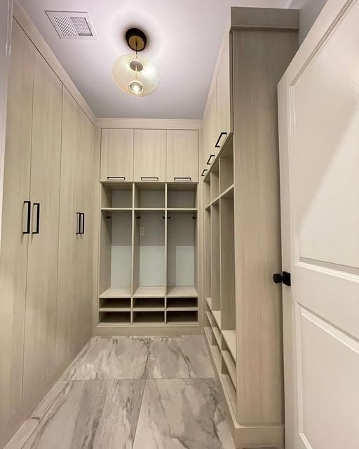 A walk-in closet with light wood cabinets, open shelves, and marble flooring.