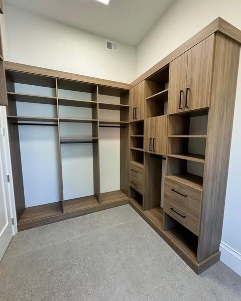 Built-in wooden closet with open shelves, hanging rods, and drawers in a corner. Light beige walls and gray carpet.