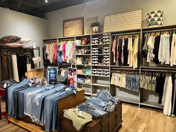 Clothing boutique interior with racks of clothes, shelves of shoes, and denim display.